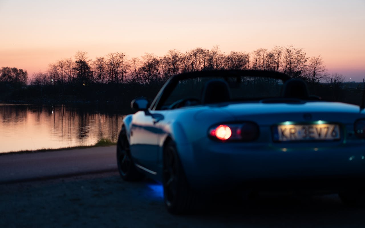 A blue convertible sports car parked by a serene lakeside during dusk in Brzegi, Poland.