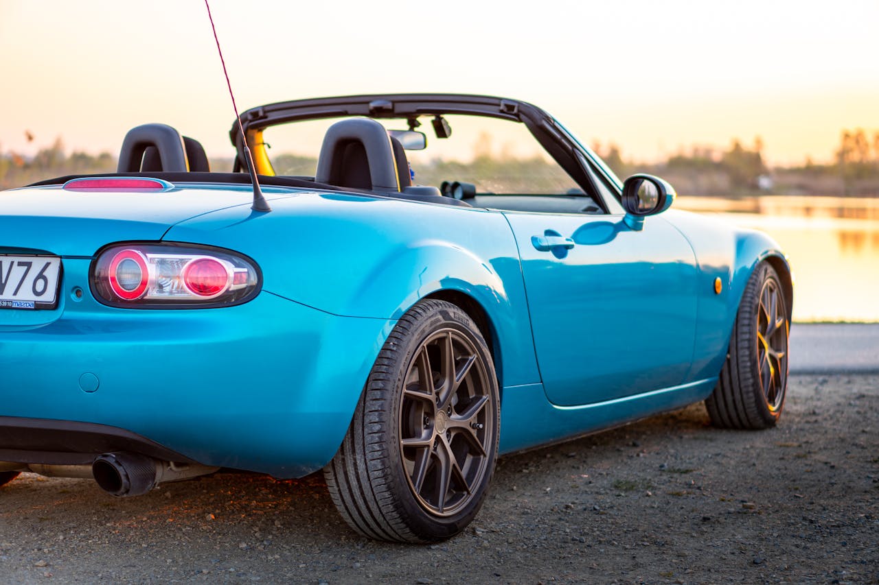 Capture of a blue Mazda MX-5 convertible sports car parked by a serene lakeside at sunset in Brzegi, Poland.